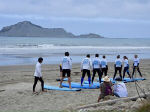 Surfing for Farmers NHB Photo of a group of people on the beach standing next to surfboards - Surfing for Farmers Hawke's Bay