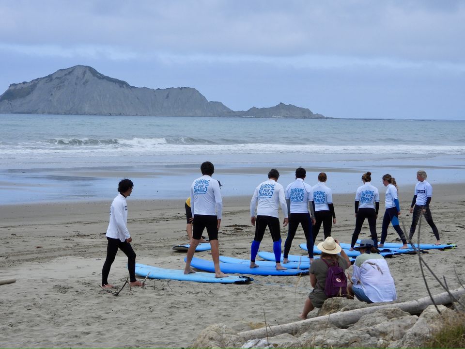 Surfing for Farmers NHB Photo of a group of people on the beach standing next to surfboards - Surfing for Farmers Hawke's Bay